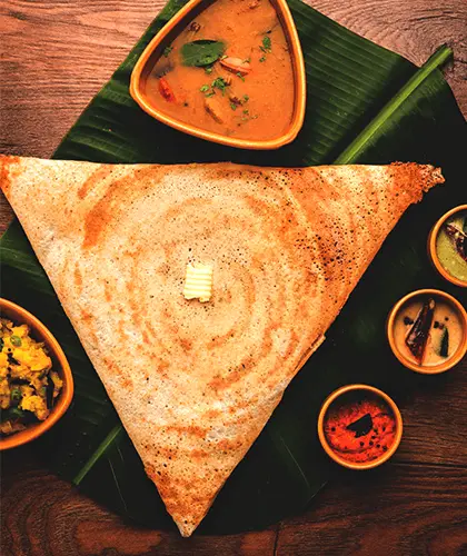 A crisp golden dosa folded on a banana leaf, with sambar and three chutneys alongside