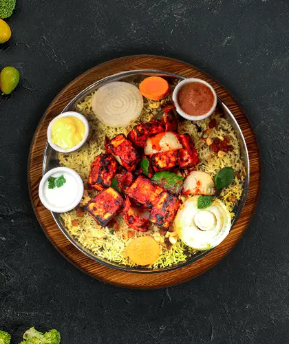 Paneer tikka and biryani on a wooden thali, with raita, chutney and sliced onion