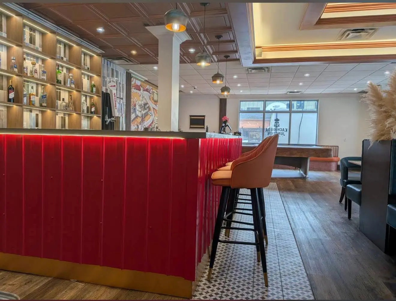 The bar — red fluted panelling and a brass kick rail, tan leather stools along the counter, spirits lit on open shelves behind